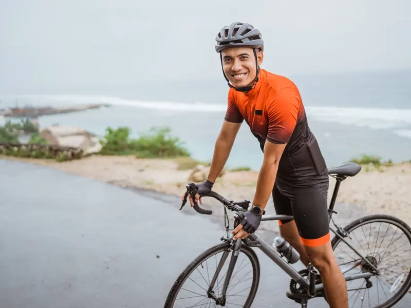 A smiling road cyclist in an orange jersey paused on a sunny coastal road