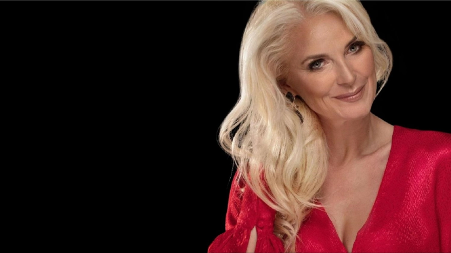 A confident woman in her fifties with long blonde hair, in a red top, smiling