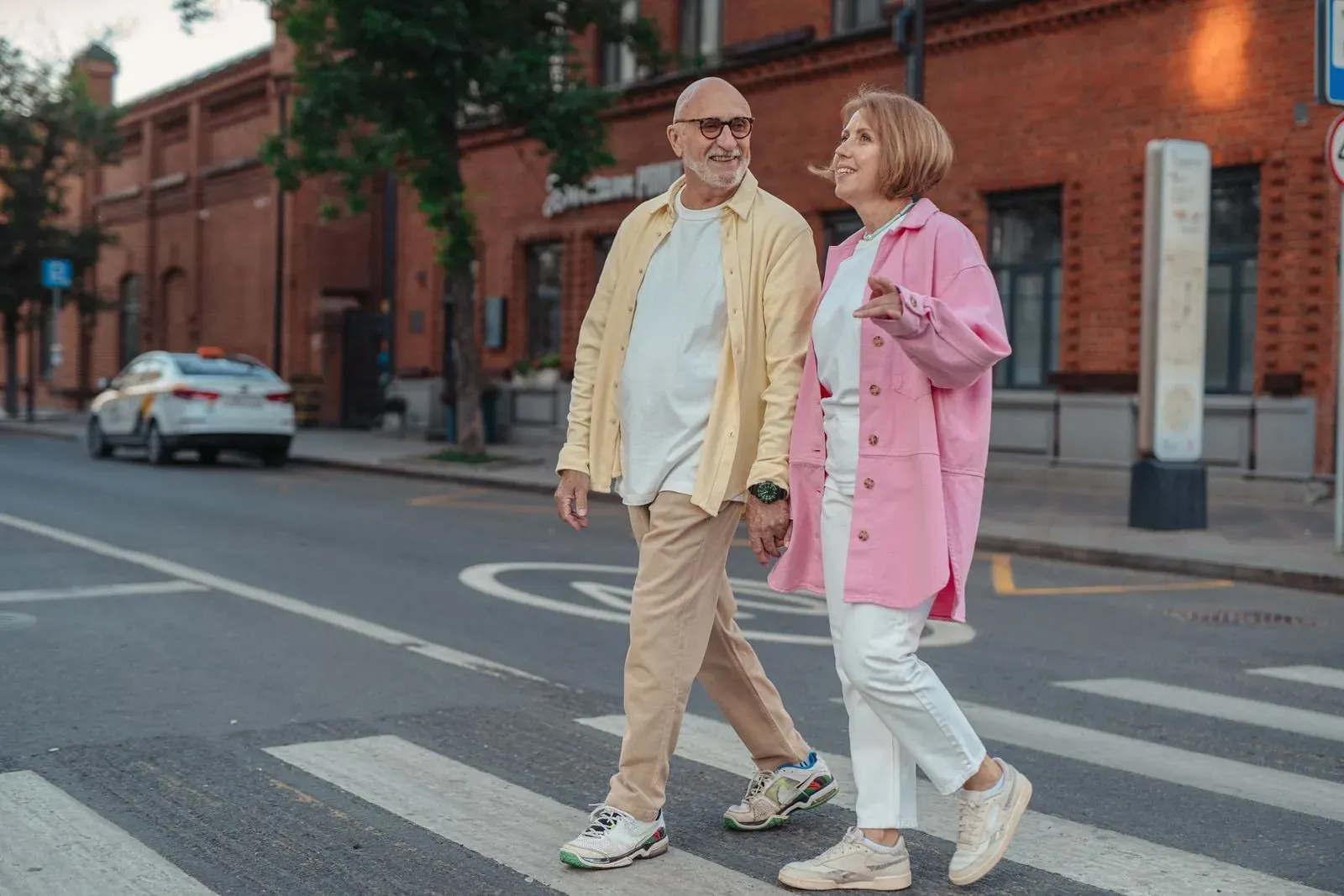 A stylish couple laughing as they cross a street lined with red-brick buildings