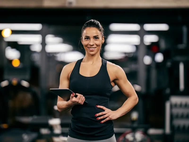 A smiling female personal trainer holding a tablet in a gym