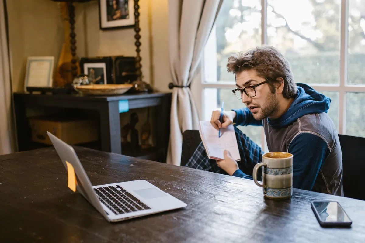 Man reading his laptop and taking notes at a desk, illustrative photo of a model