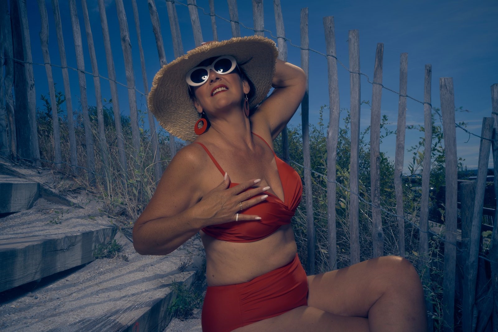 Glamorous mature woman in a red swimsuit and wide straw hat at the beach