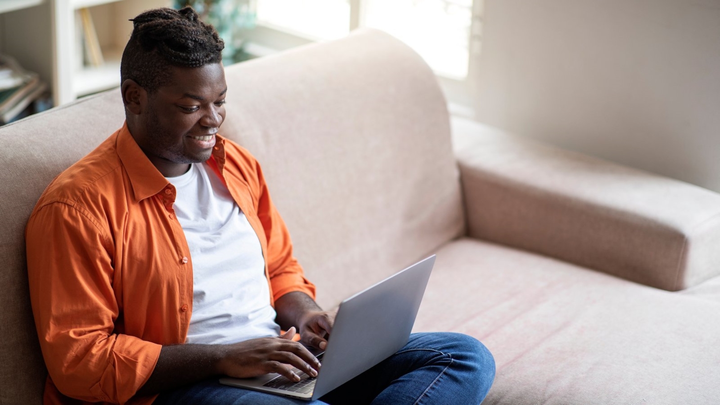 A man smiling while using his laptop on the sofa