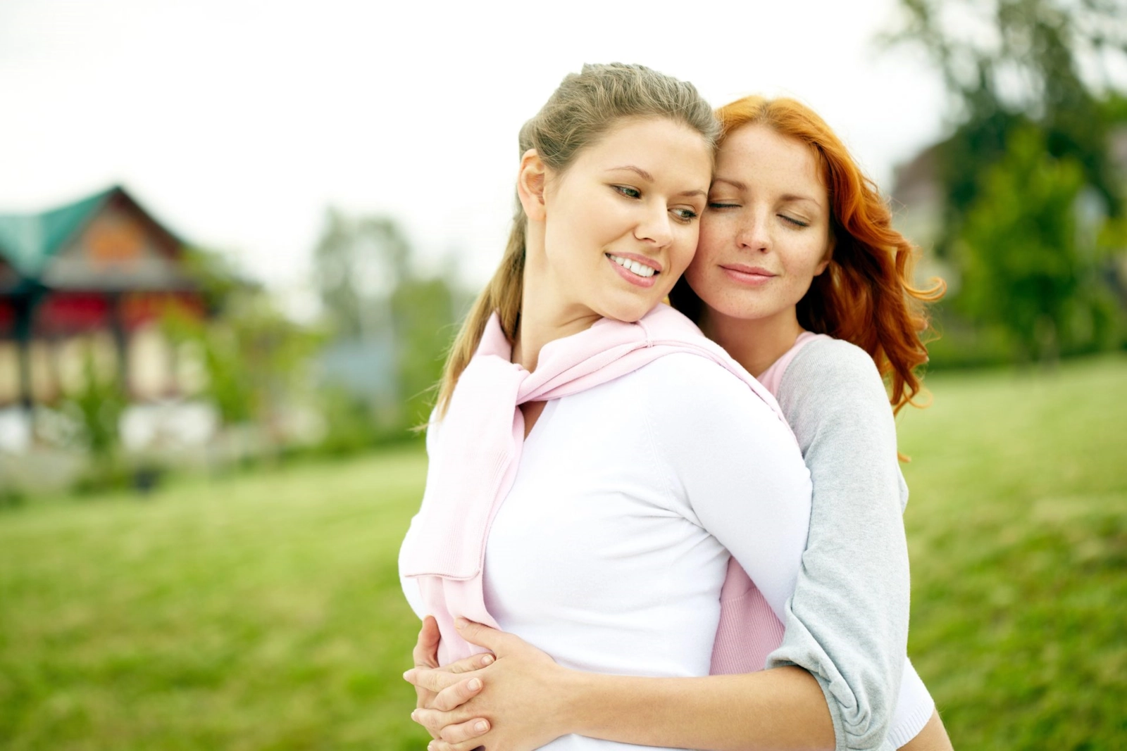 Two women in a close embrace outdoors, one with her eyes closed