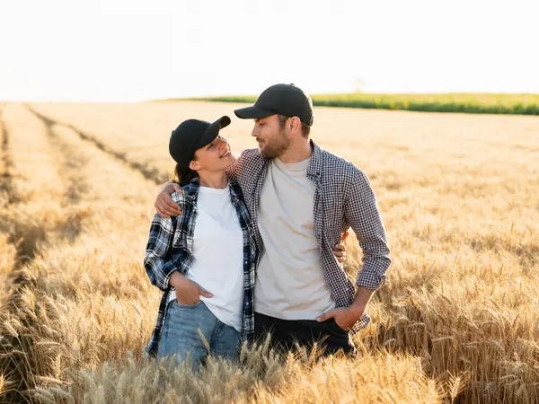 A couple standing together at the edge of a wheat field in the evening