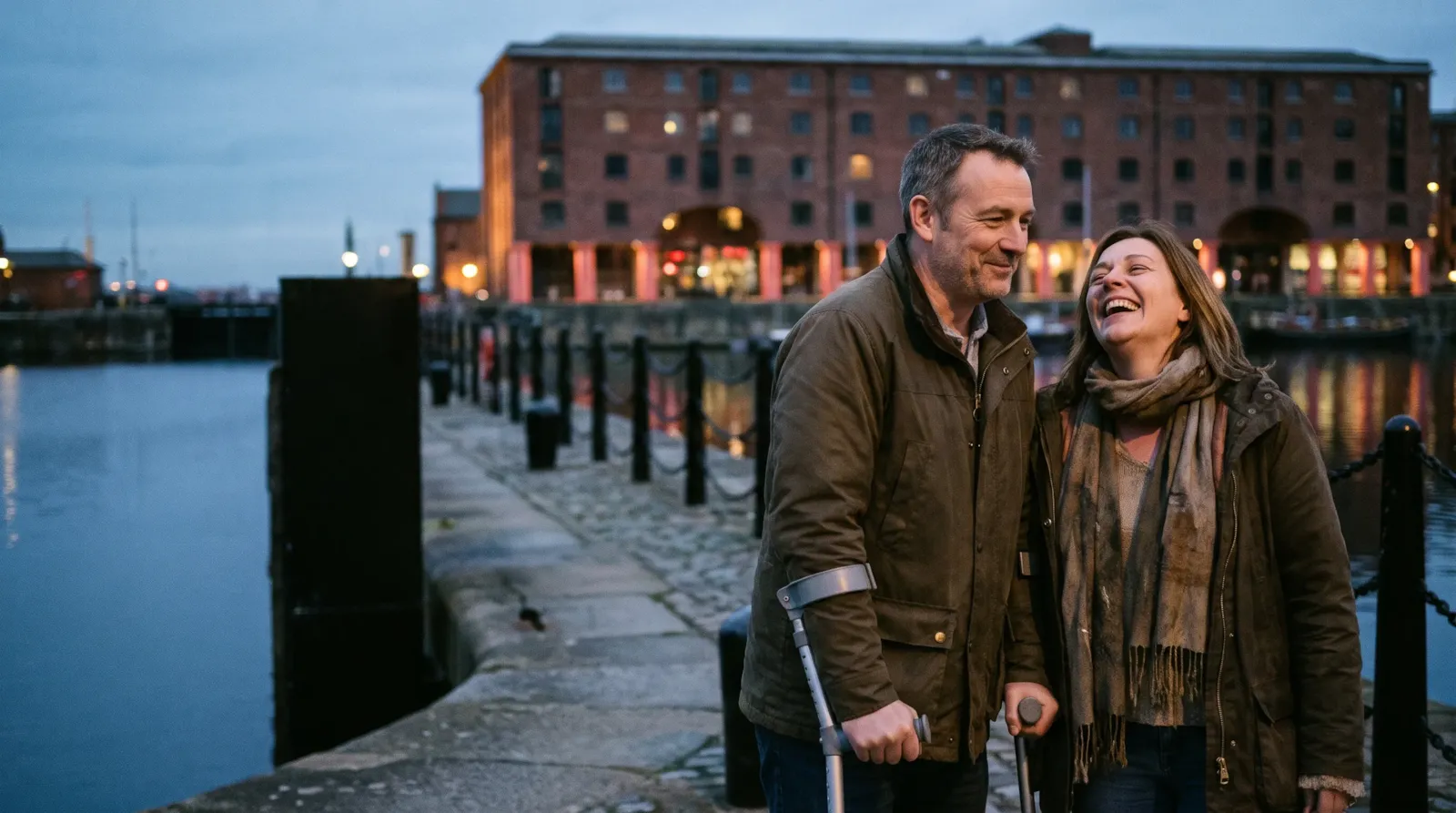 A couple laughing on the quayside at the Royal Albert Dock in Liverpool; the man walks with forearm crutches