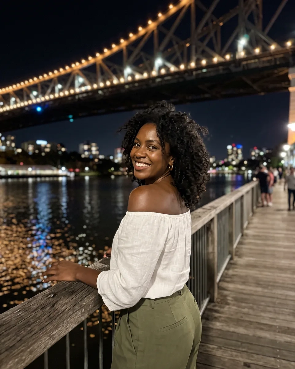 A woman with loose black curls in an off-the-shoulder white top glances back with a grin on a riverside boardwalk beneath the lit Story Bridge in Brisbane at night (AI-generated image)