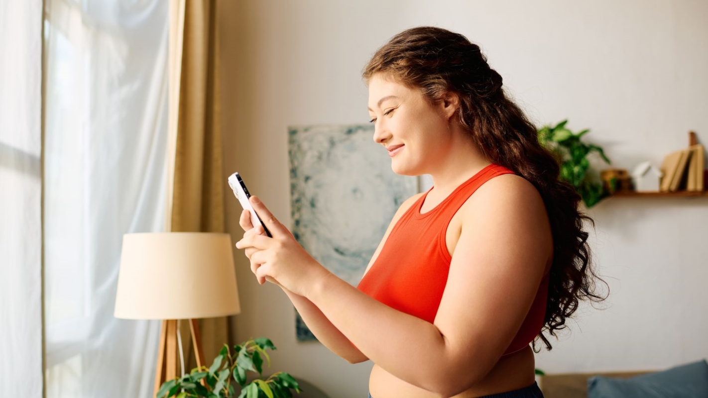 A woman smiling at her phone while sitting on a cosy sofa