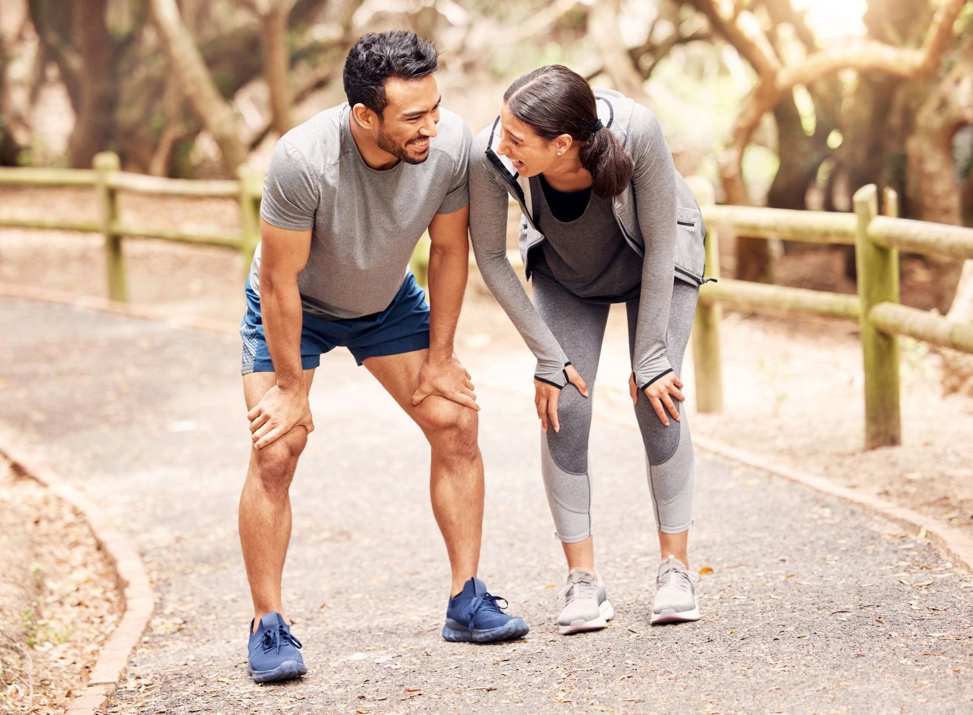 A laughing man and woman catching their breath together on a tree-lined running path