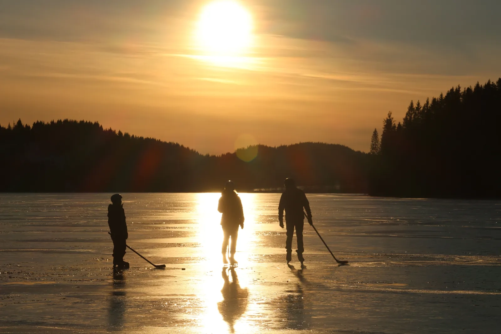 Skaters gliding across frozen water at sunset with a treeline in the distance