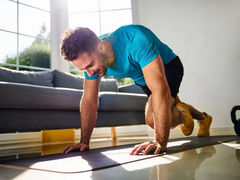 A man doing a mountain-climber workout on a mat in his sunny living room