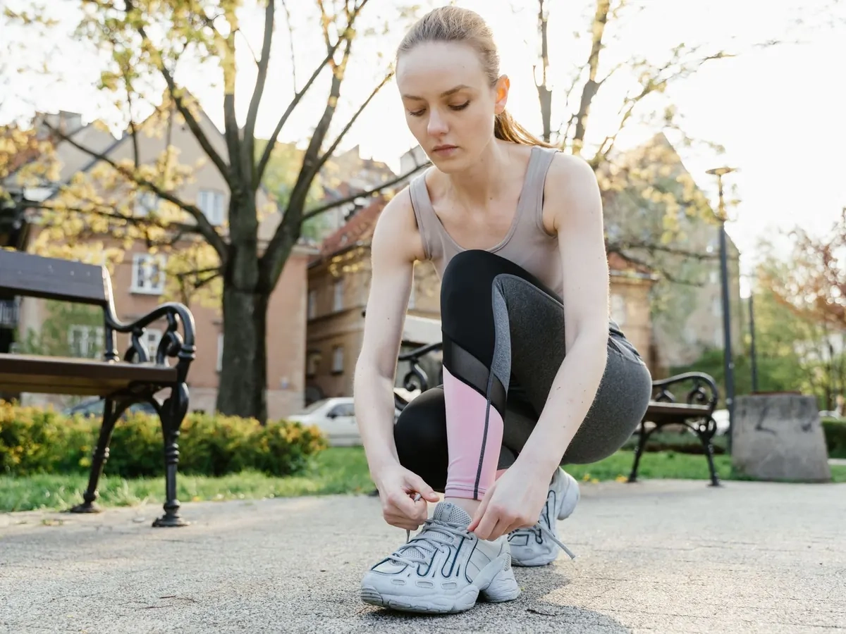 Woman in activewear tying her running shoes in a park, illustrative photo of a model
