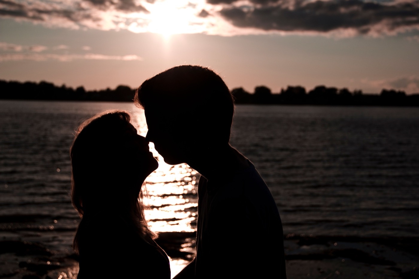 A couple stands in silhouette on a shore at sunset