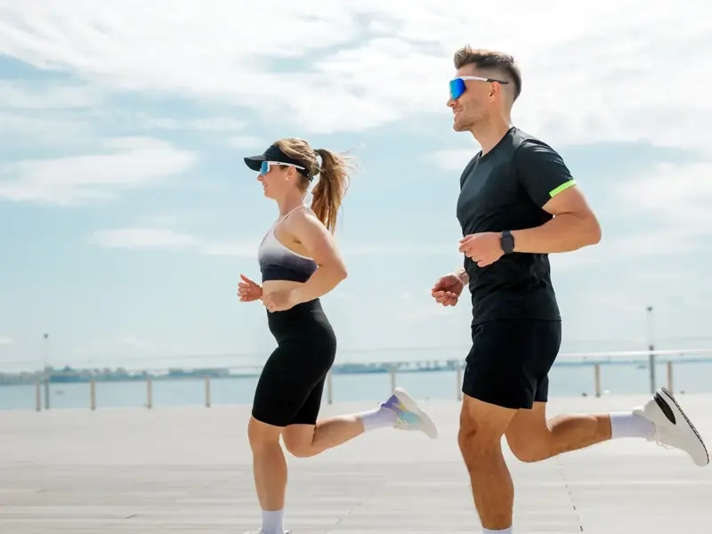 A man and woman running side by side along a sunny seaside promenade