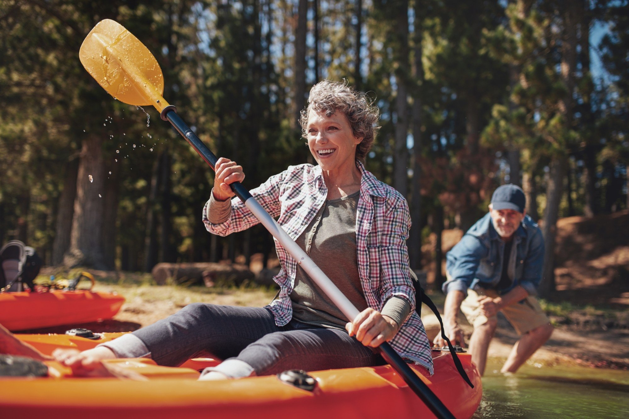 A laughing woman paddling a kayak as a man pushes her off from the lakeshore