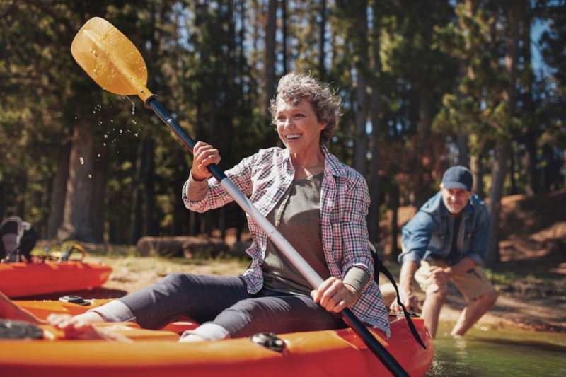 A laughing woman paddling a kayak as a man pushes her off from the lakeshore