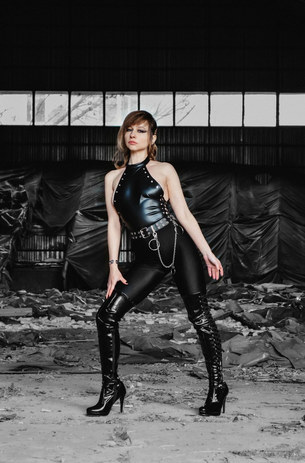 Woman in black latex and thigh-high boots standing in an industrial space, black and white stock photo