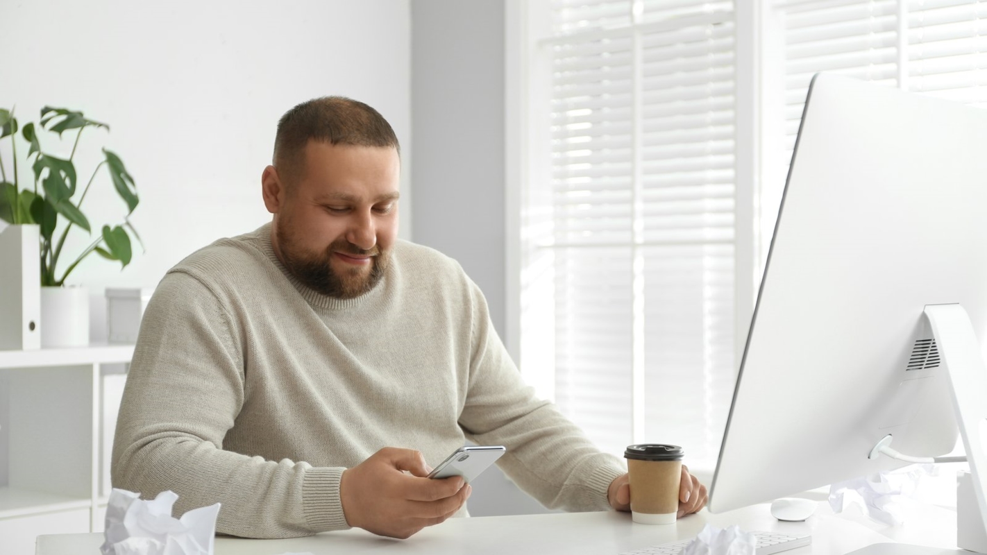 A man looking thoughtfully at his phone at his desk
