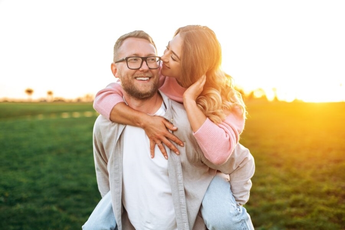 Couple in a field at golden hour, woman kissing man on the cheek