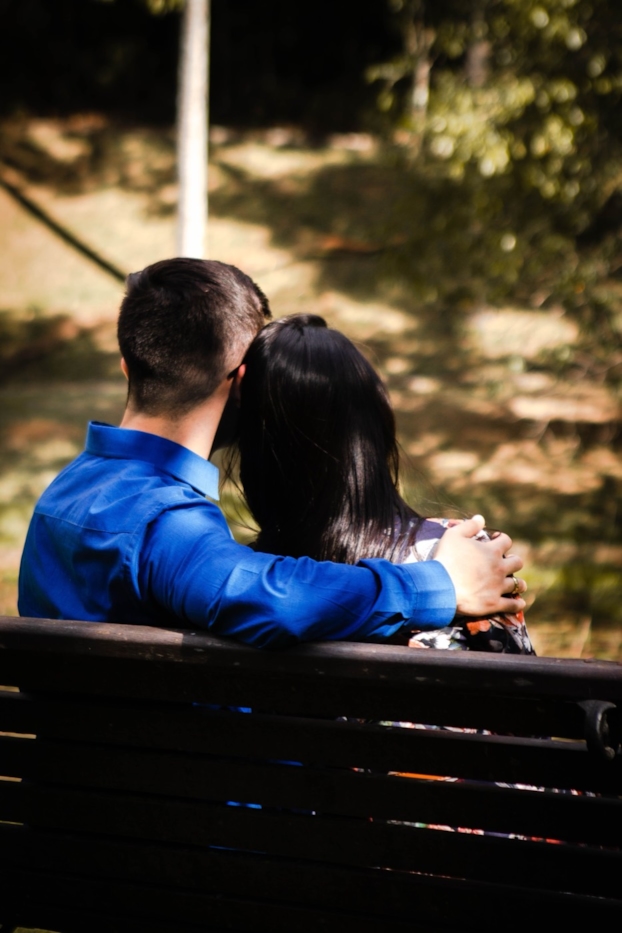 A couple shares a hug on a bench, seen from behind