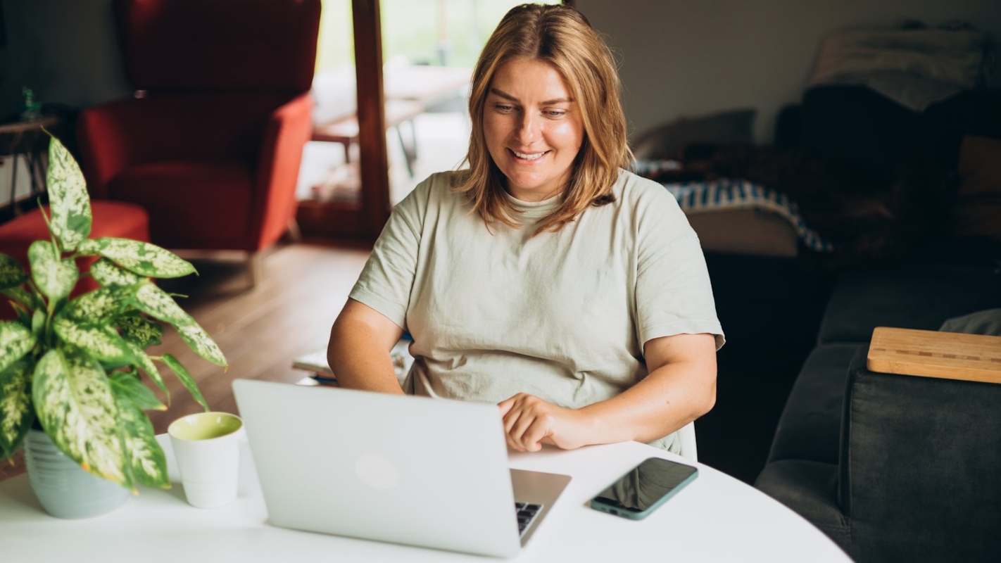 A woman smiling while working on her laptop at home