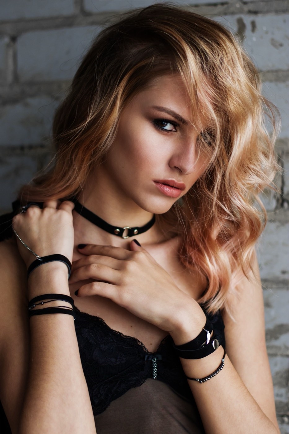 Illustrative stock photo of a blonde woman in black lace lingerie and a ring choker against a brick wall. Does not depict real members.