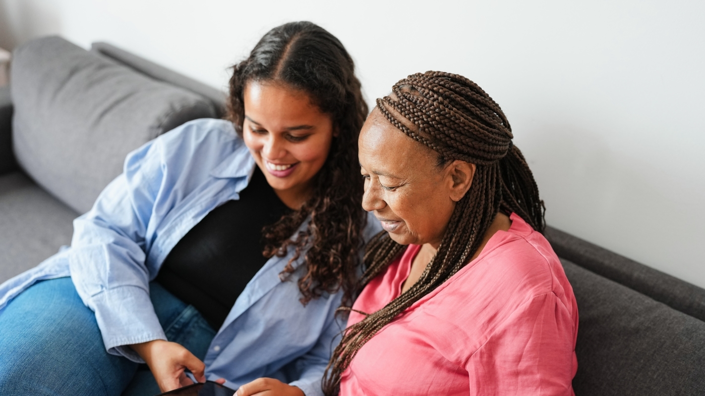 Two friends sitting together on a sofa, smiling as they look at a phone
