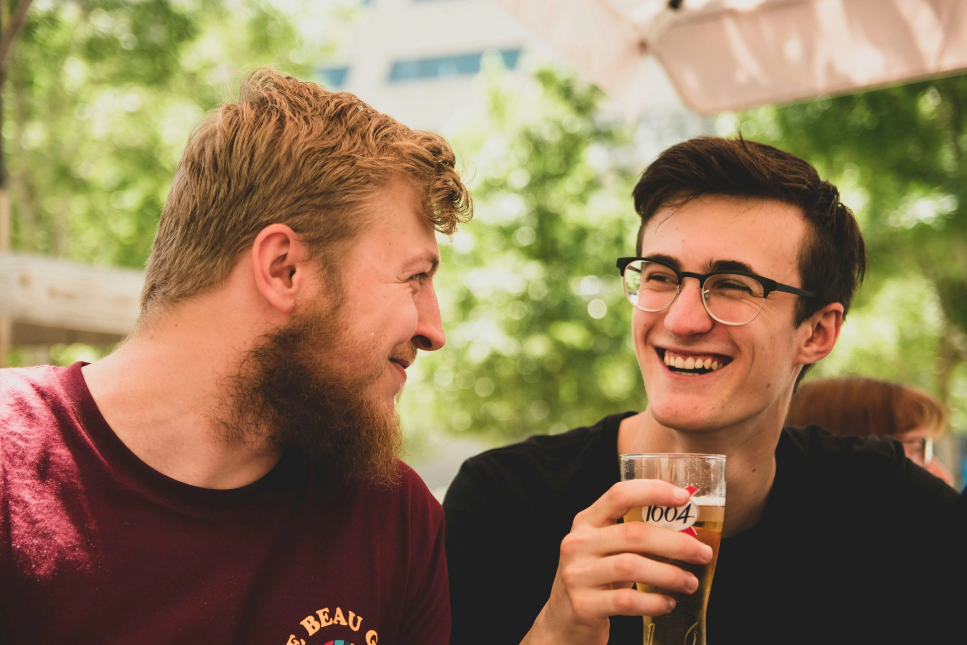 Dos hombres riéndose con una cerveza en la mano.
