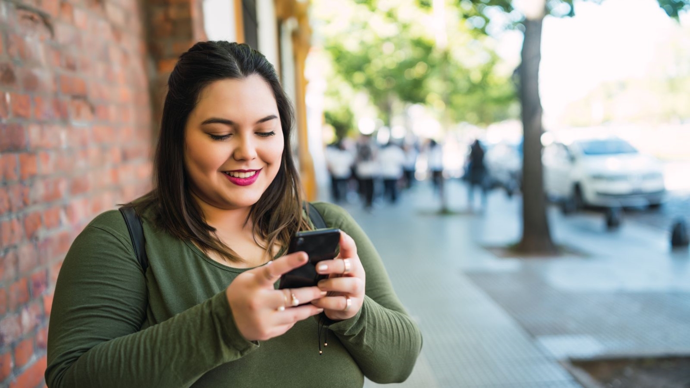 A woman smiling as she checks her phone on a city street
