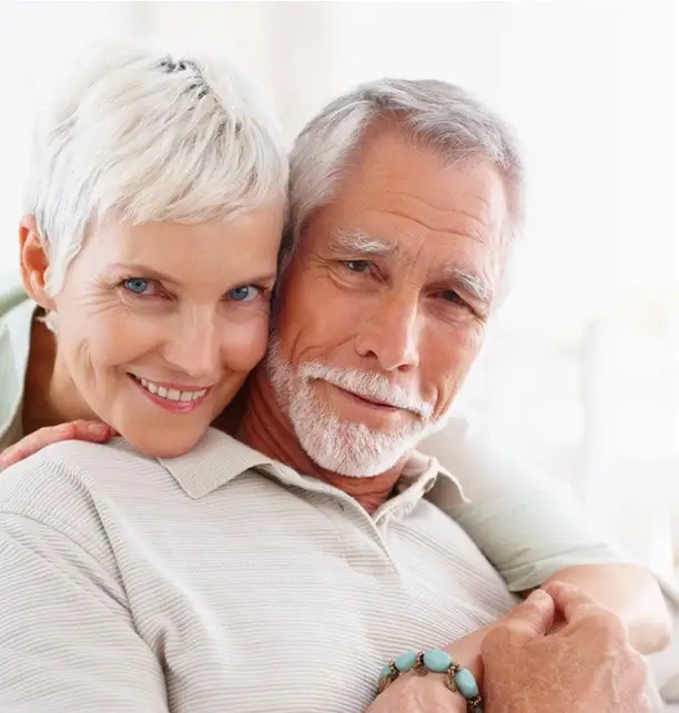 A smiling grey-haired couple, his arms wrapped around her shoulders