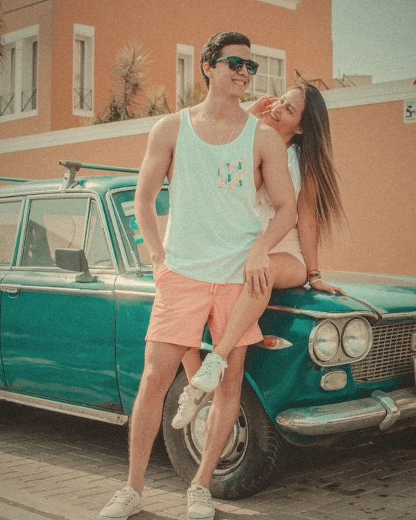 Couple sitting on the bonnet of a vintage teal car
