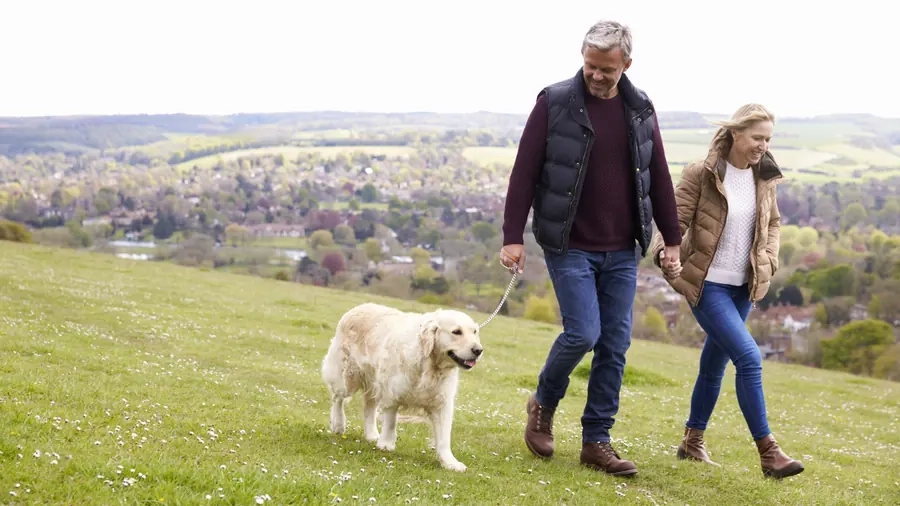 A couple walking a white dog along a hillside path above a village