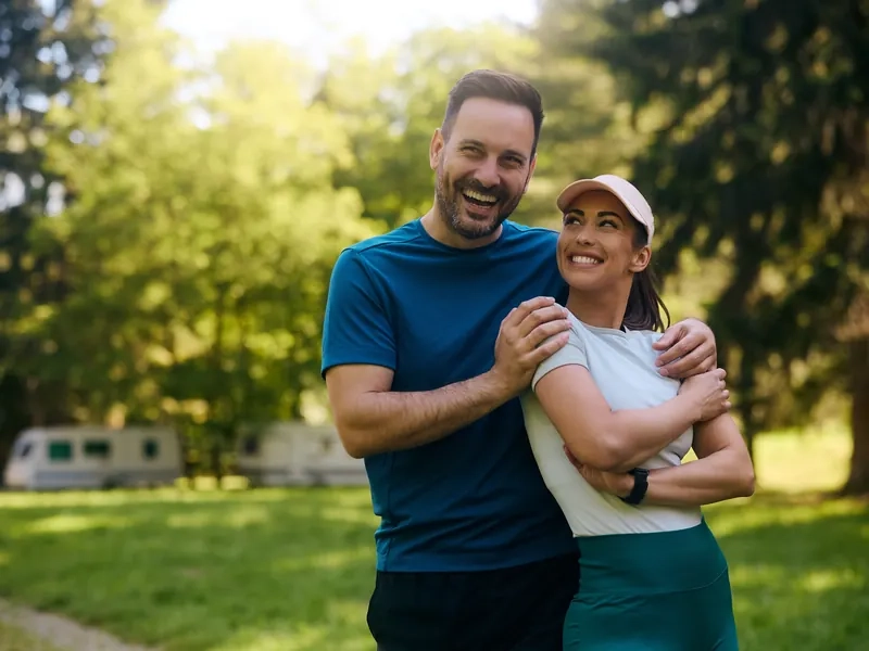 A happy couple in workout clothes hugging and smiling in a sunny park