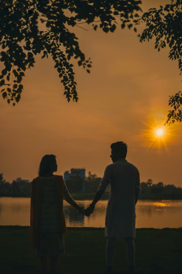 A couple holds hands beside a lake at sunset