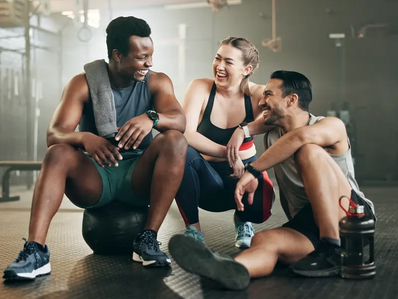 Three friends laughing together on the gym floor after a class