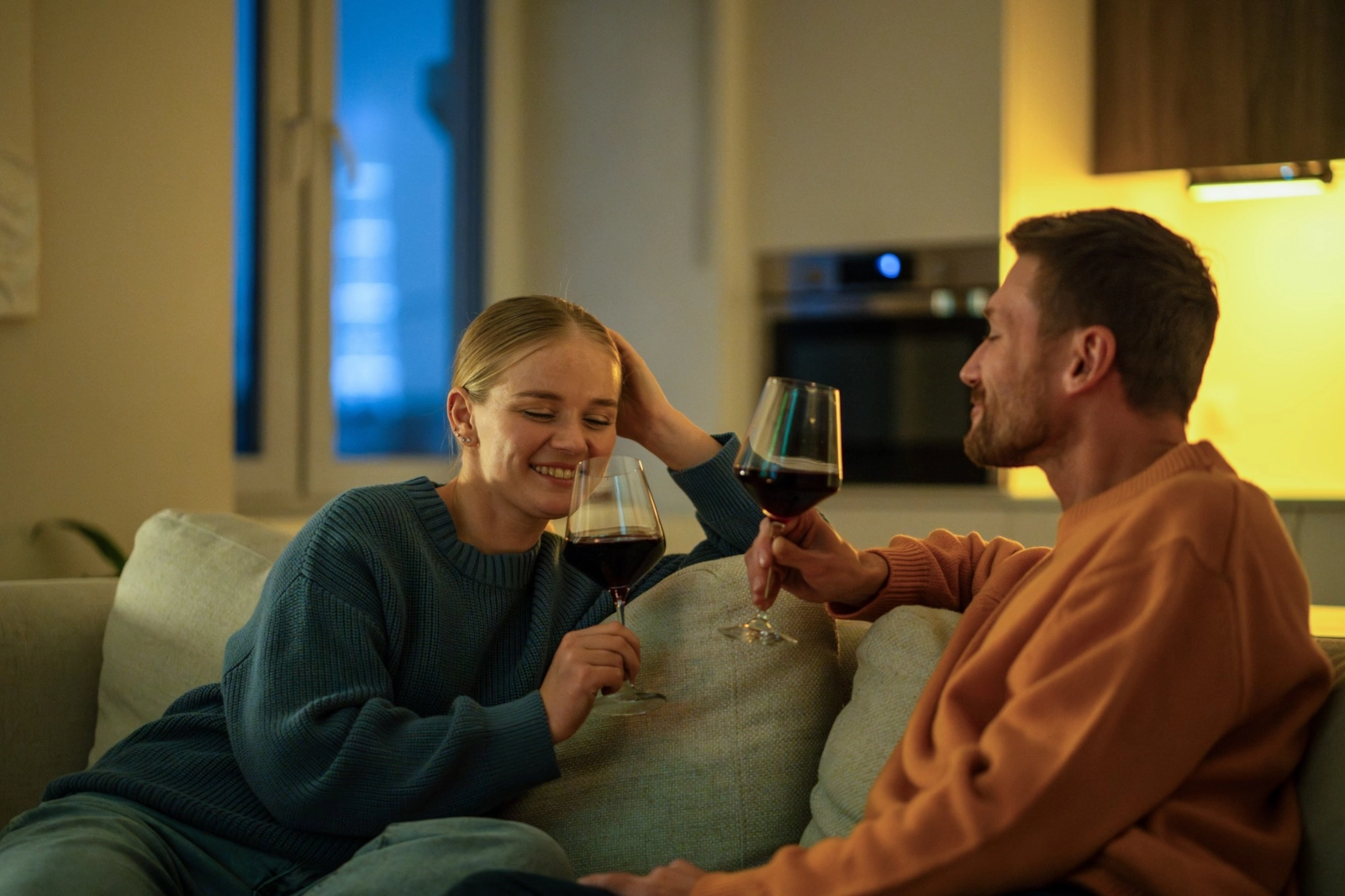 A couple laughing together on a sofa with glasses of red wine
