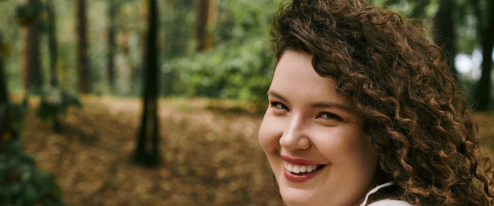 A curvy woman with curly hair smiling outdoors