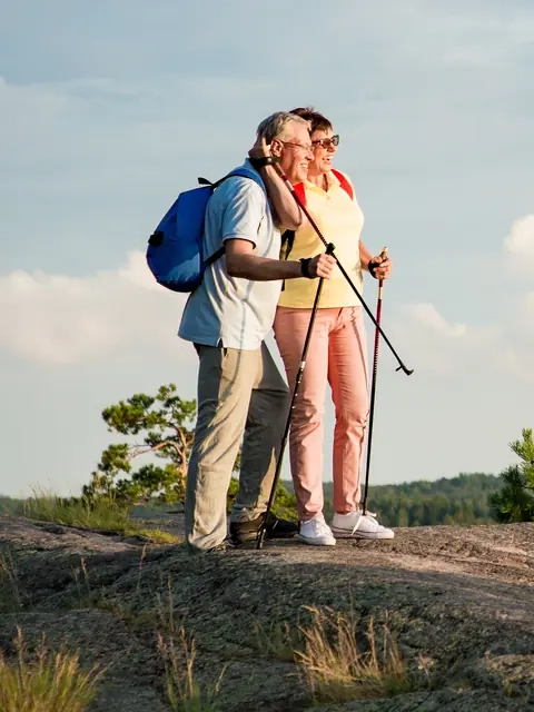 An older couple with hiking poles enjoying the view from a rocky lakeside summit