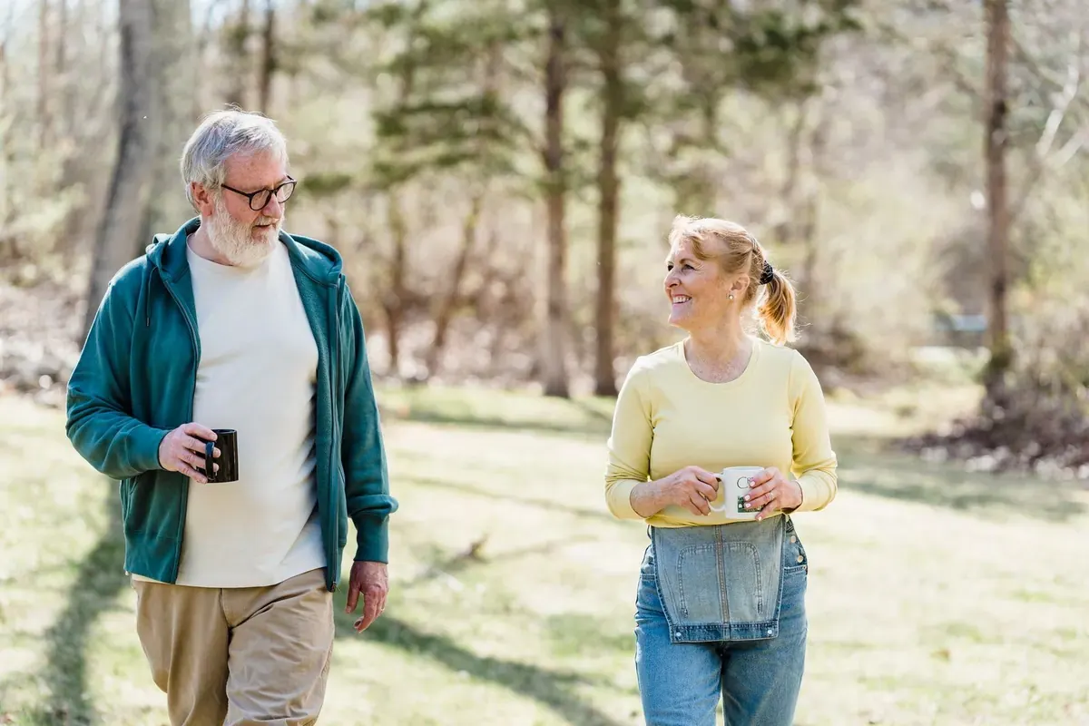 A couple walking through a park with coffee mugs, smiling at each other
