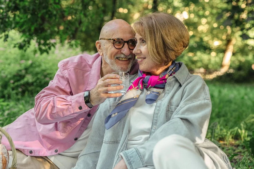 An older couple sitting close together on the grass in a park, laughing