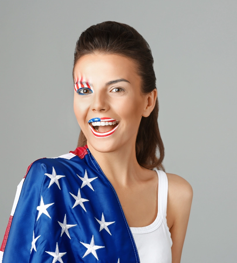 A smiling woman with stars and stripes painted on her cheek, wrapped in the American flag