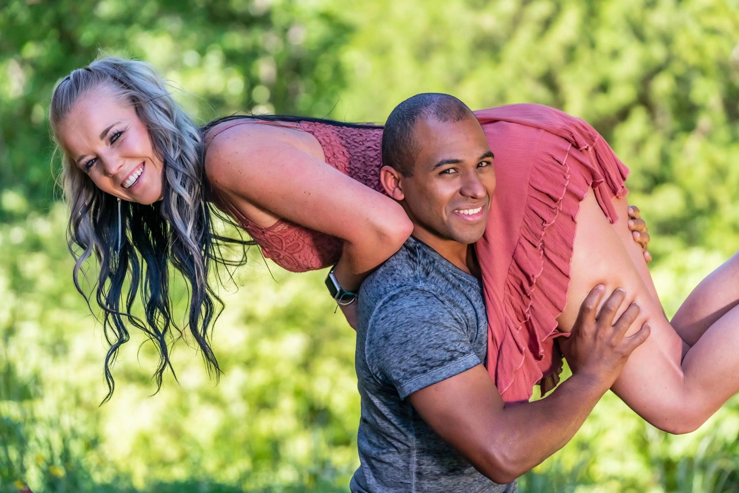A woman laughing as a man lifts her onto his shoulders on a sunny lawn