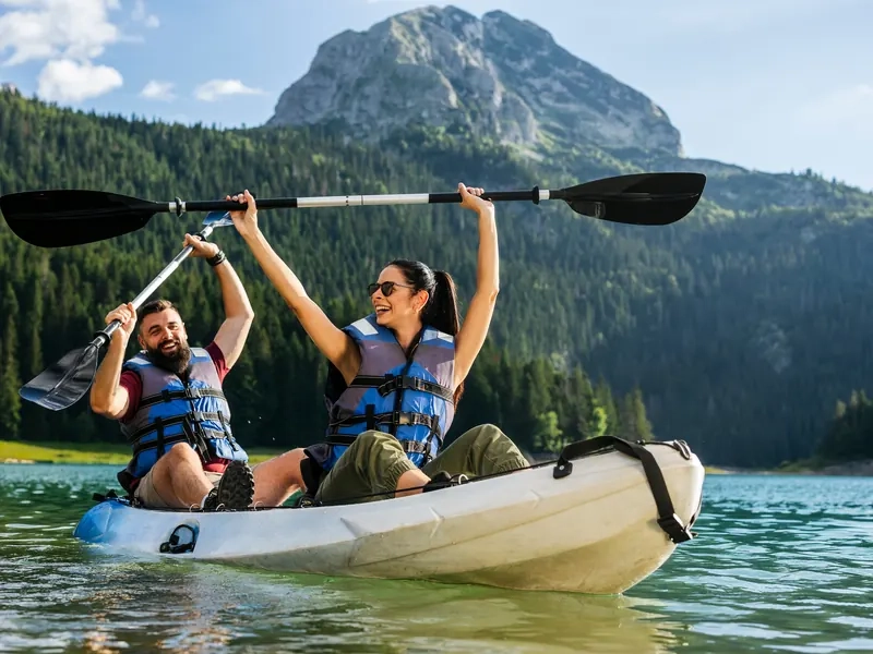 A couple raising their paddles in celebration while kayaking on a mountain lake