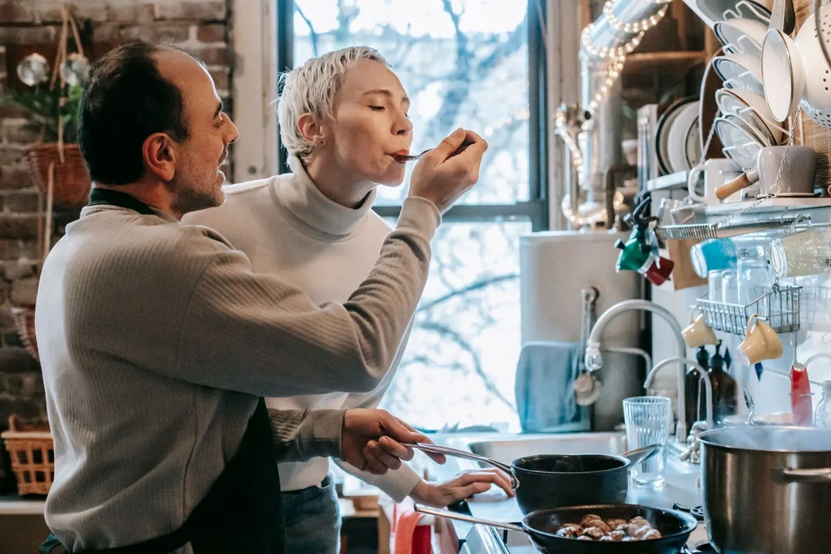 Woman tasting a dish her partner cooked in their kitchen, illustrative photo of models