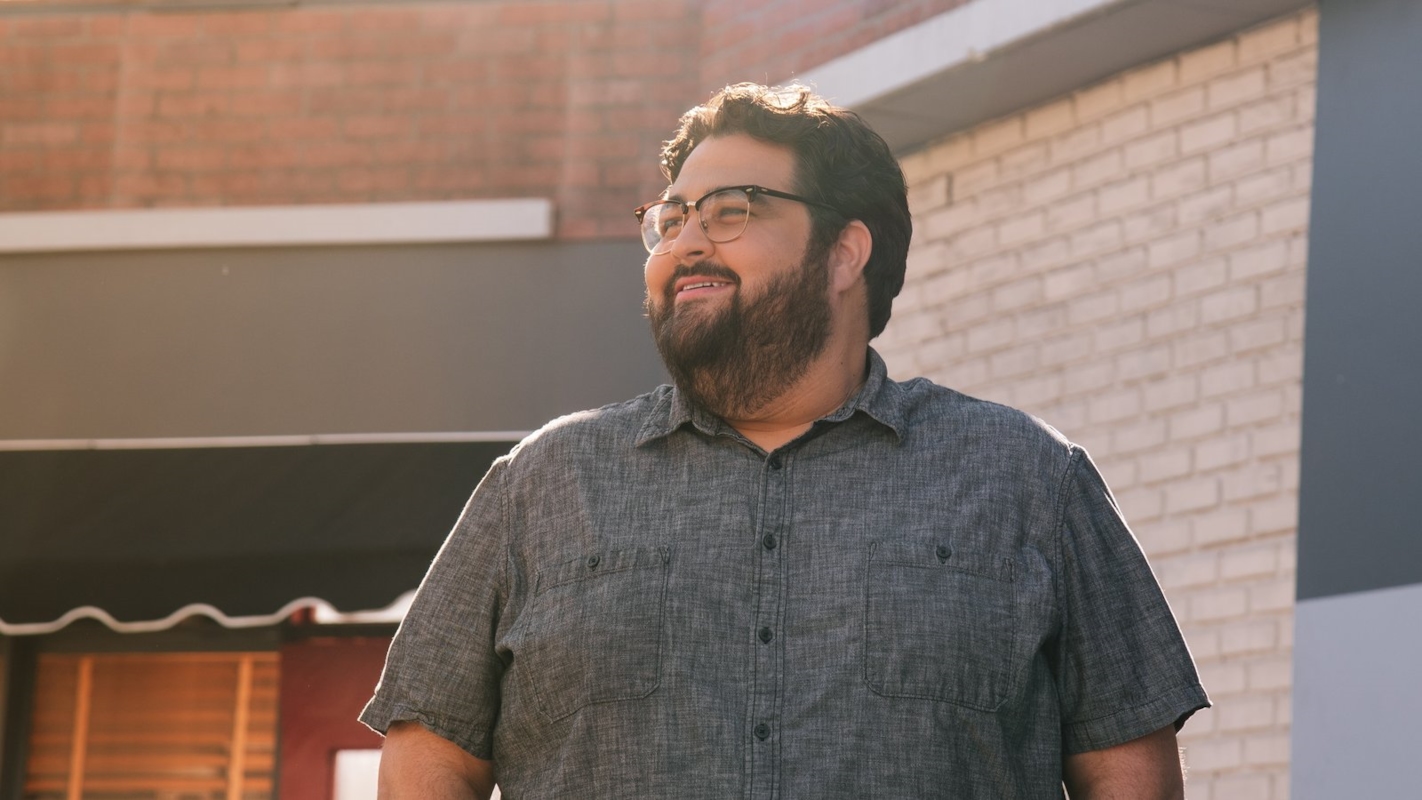 A man smiling outdoors near a brick building