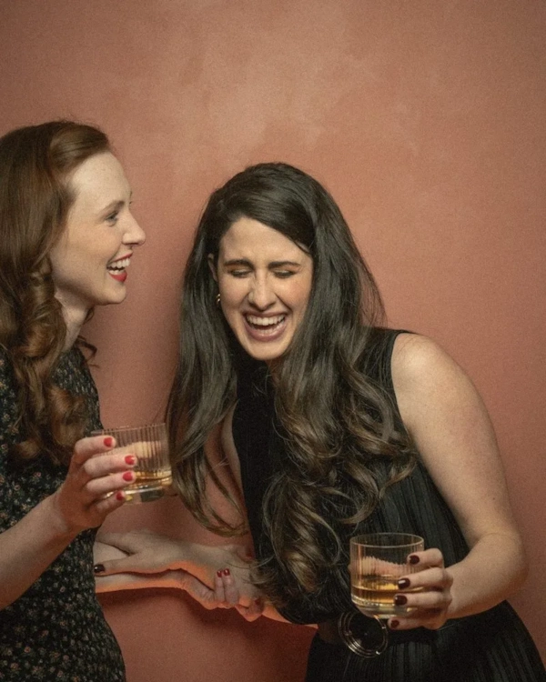 Two women laughing with drinks in hand