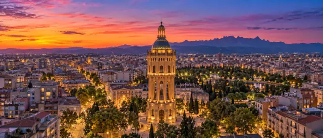 Sabadell al atardecer con la Torre de l'Aigua iluminada sobre los tejados y las montañas al fondo