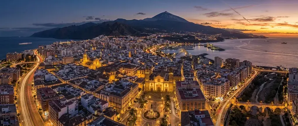 Vista aérea de Santa Cruz de Tenerife al atardecer, con la ciudad iluminada y el Teide al fondo