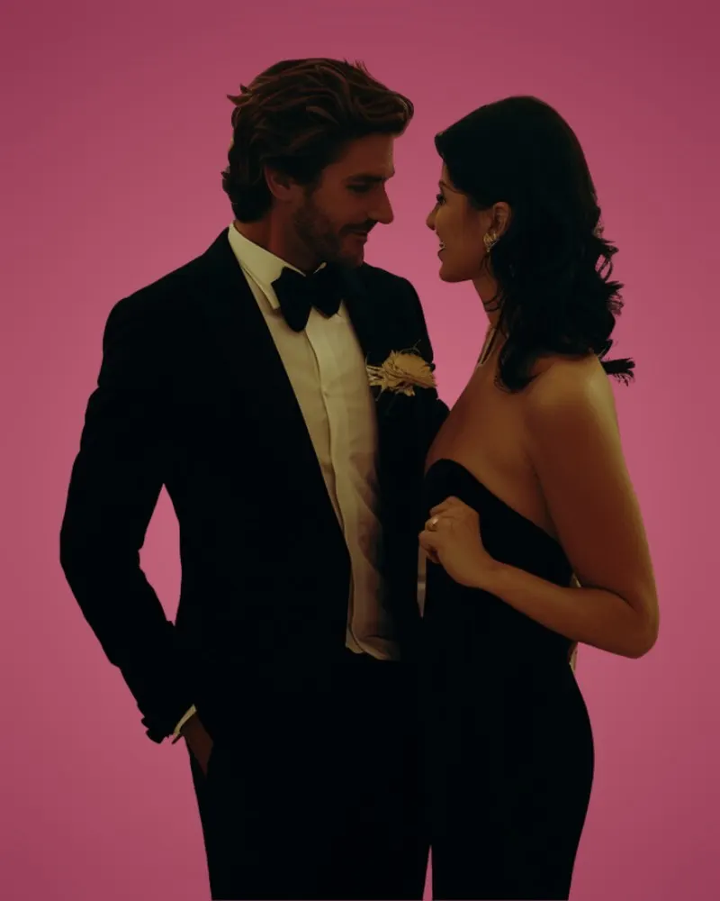 A man in a tuxedo and a woman in a strapless black dress standing close, about to kiss