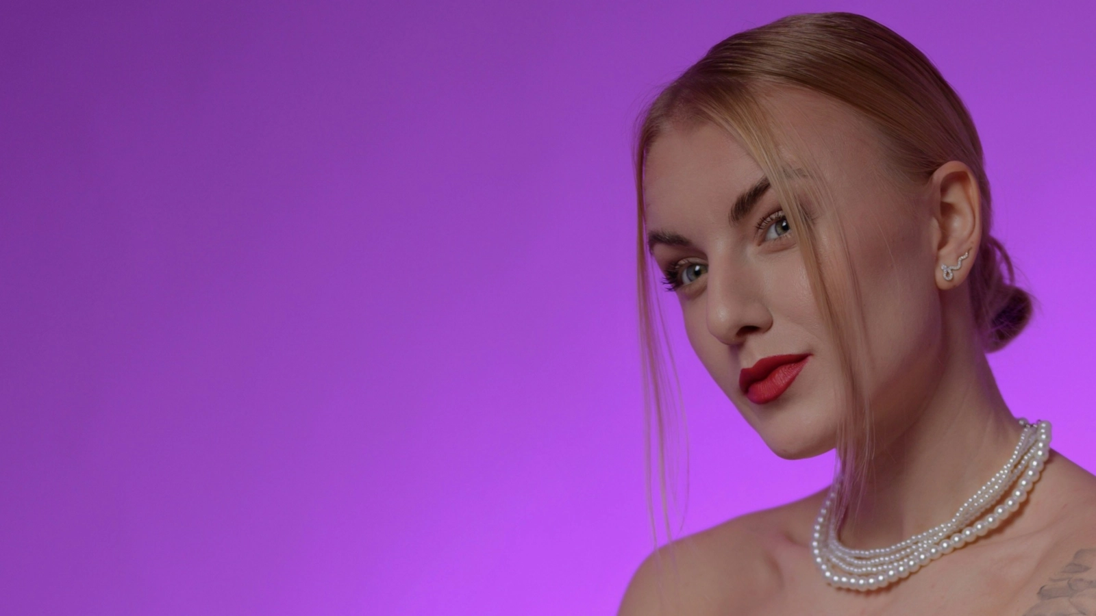 retrato de una persona rubia con el pelo recogido, labios rojos y collar de perlas, sobre un fondo morado